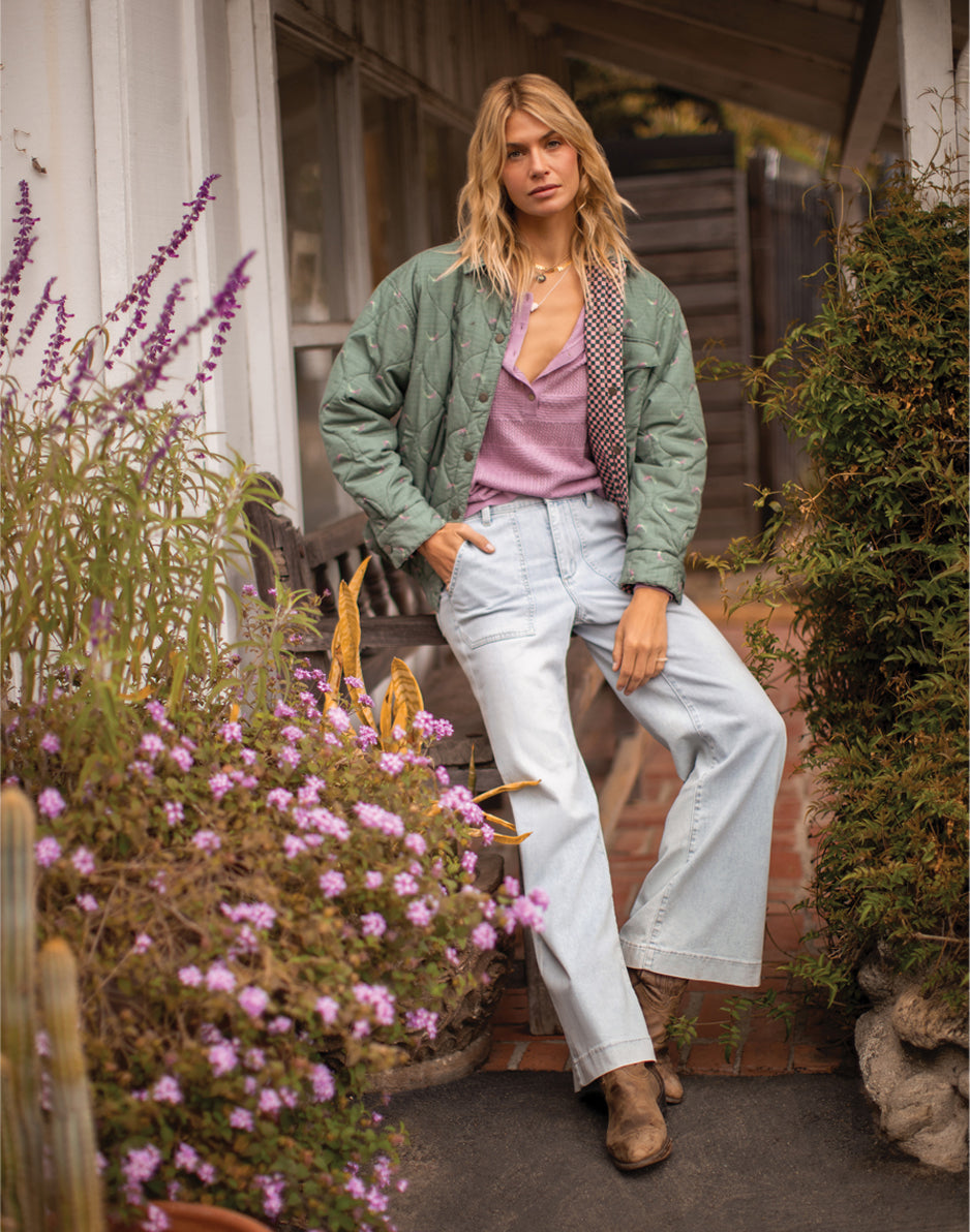 Women's quilted reversible jacket in sage green with plaid lining, worn open over pink top with wide-leg jeans