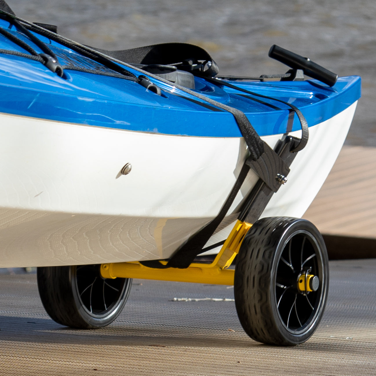Yellow kayak cart with black wheels supporting a blue and white kayak on pavement