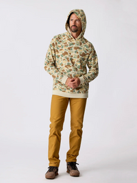 Men's camo pullover hoodie with kangaroo pocket, worn with mustard pants, full body front view