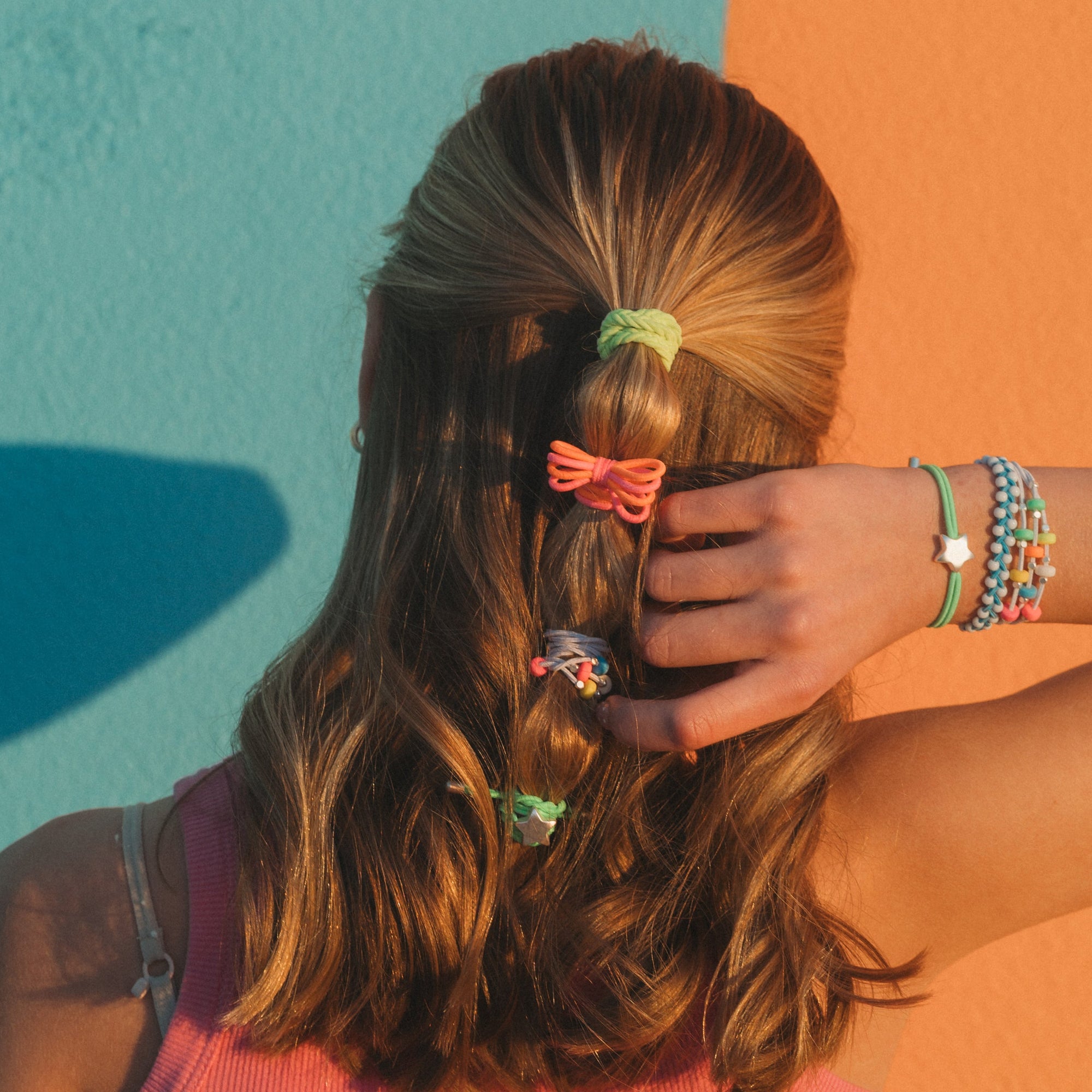Back view of model with layered hair ties and colorful beaded bracelets stacked on wrist