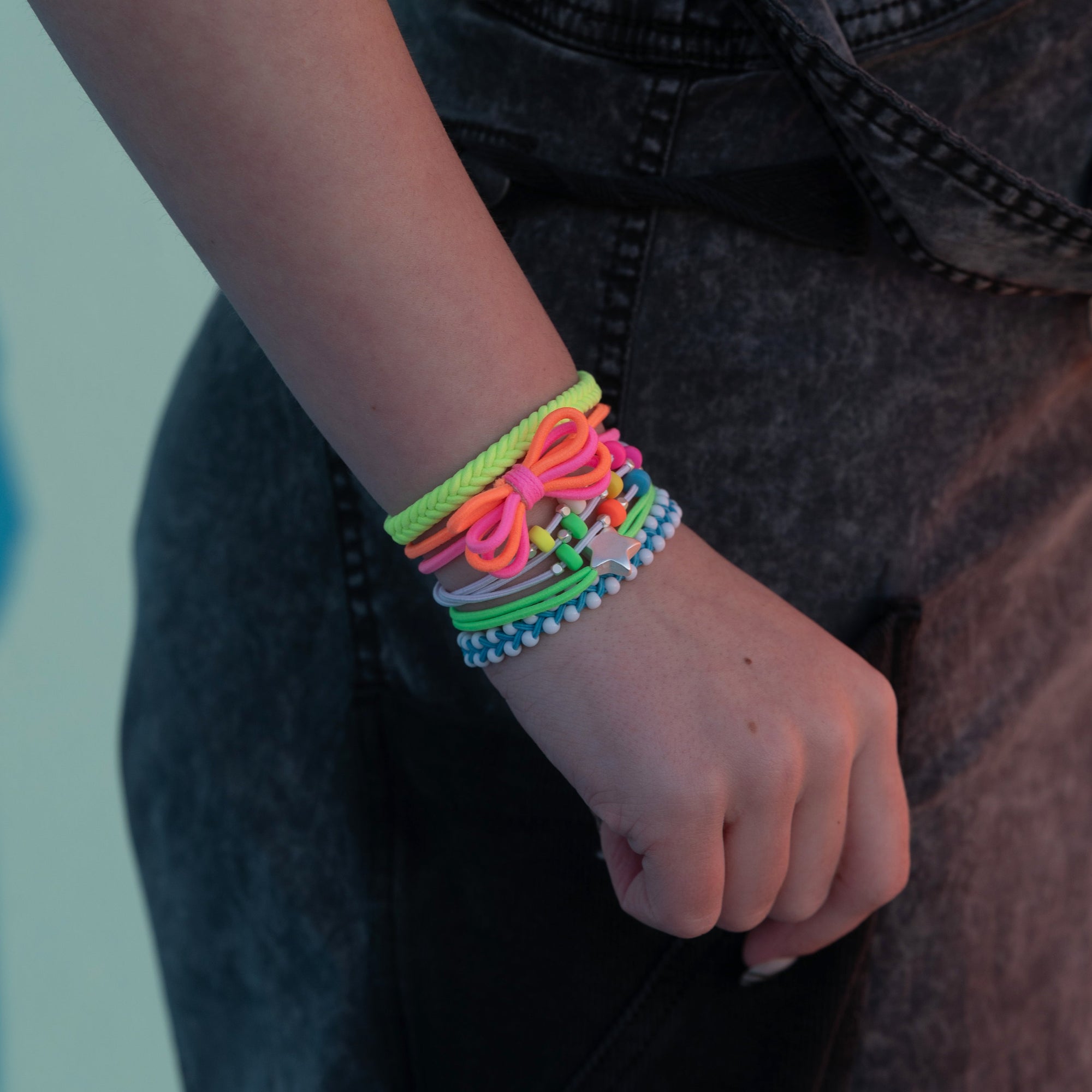 Stack of colorful neon hair tie bracelets with bow and star charm worn on wrist