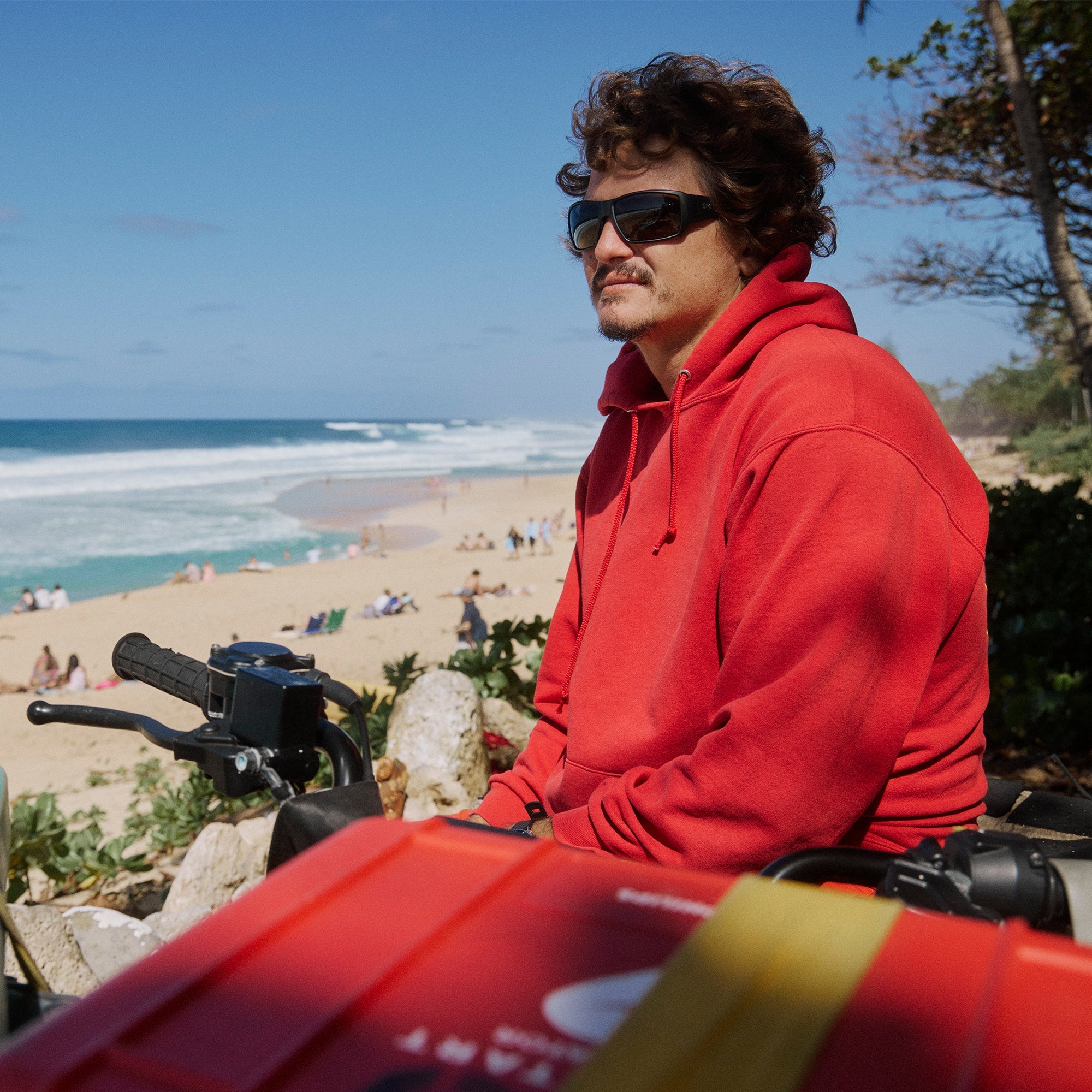 Dark sunglasses with rectangular frames worn by person in red hoodie at beach