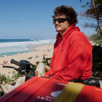 Dark sunglasses with rectangular frames worn by person in red hoodie at beach