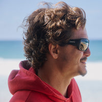 Black wraparound sunglasses worn by person in red hoodie at beach