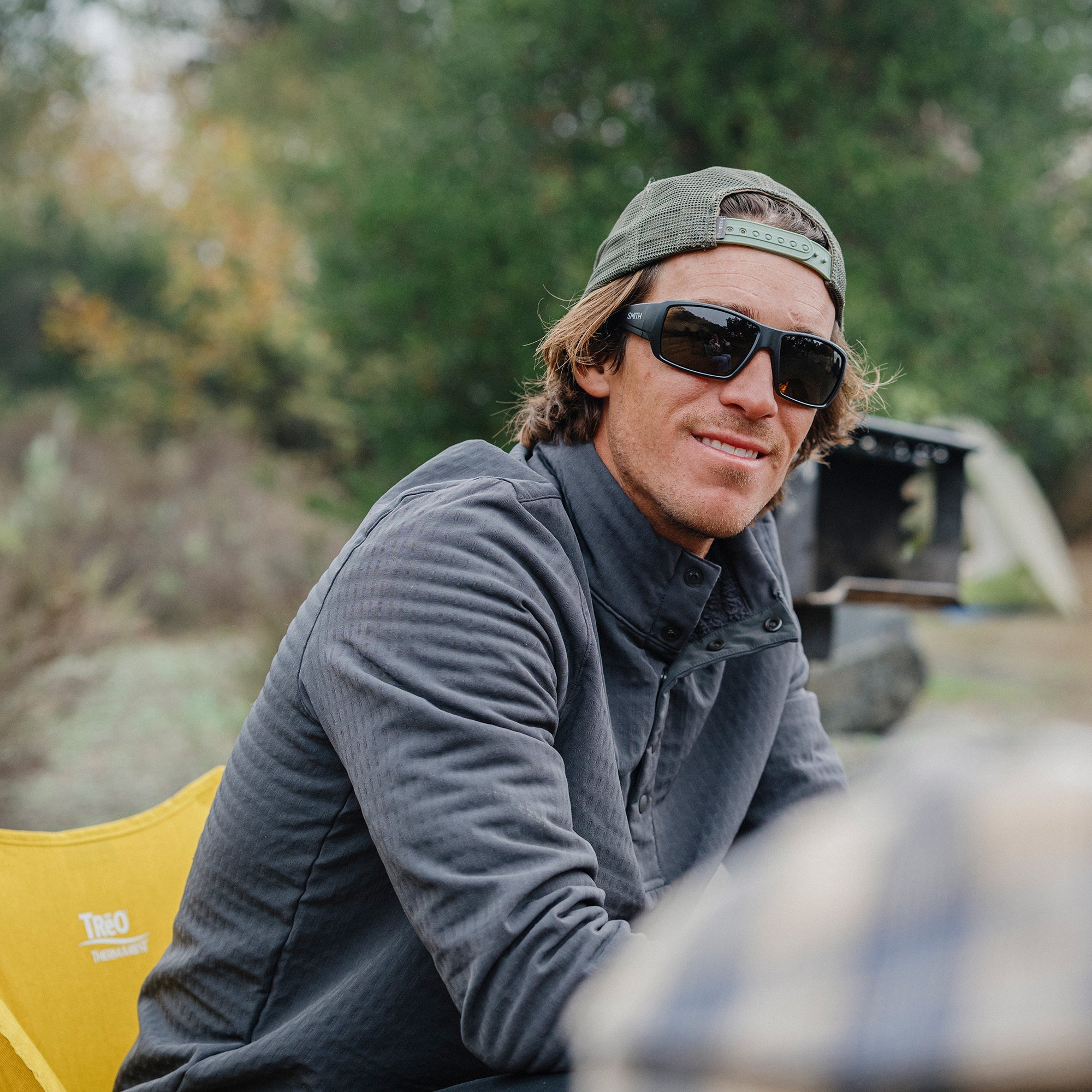 Man wearing dark rectangular sunglasses with polarized lenses in outdoor camping setting