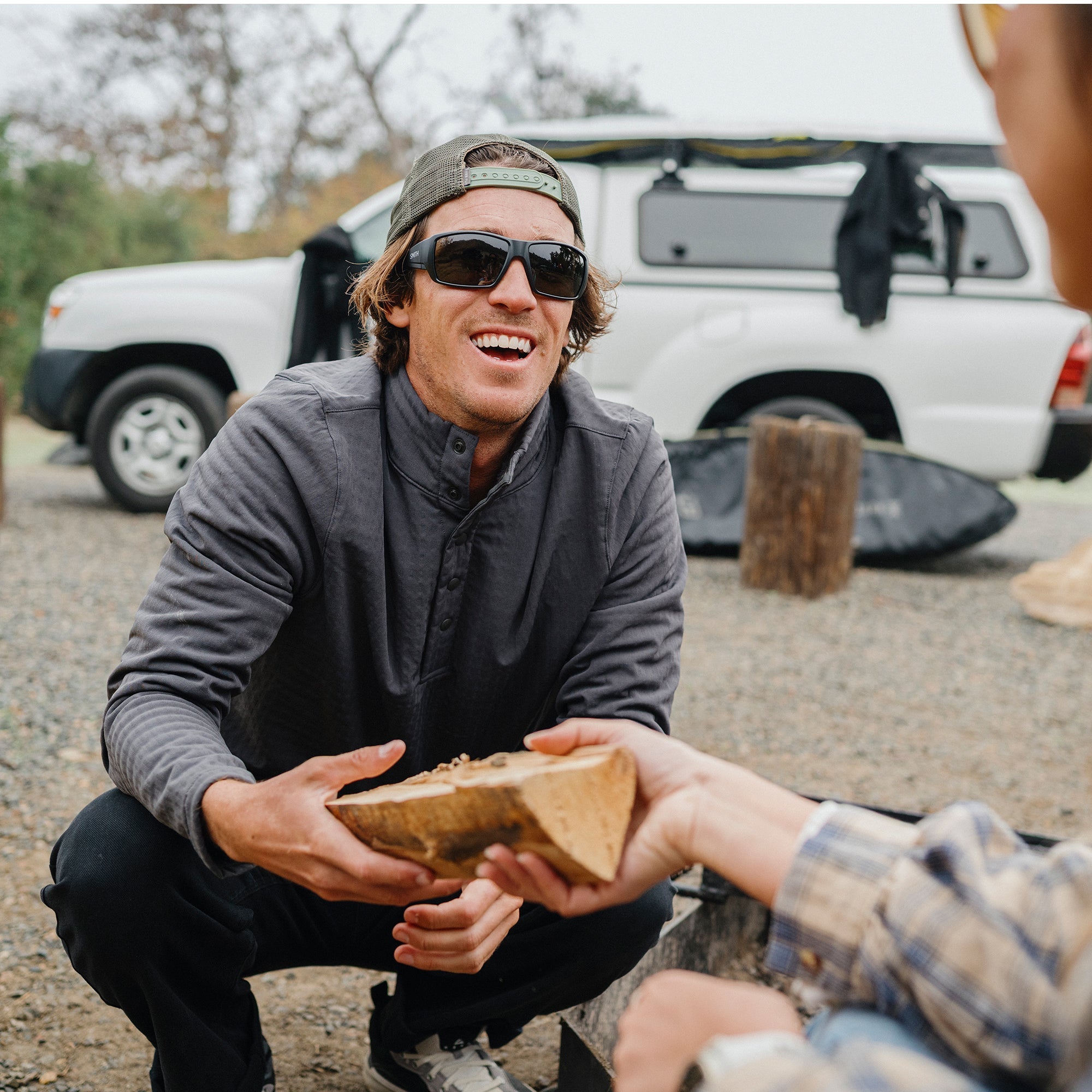 Man wearing black sunglasses outdoors while sharing food from wooden bowl