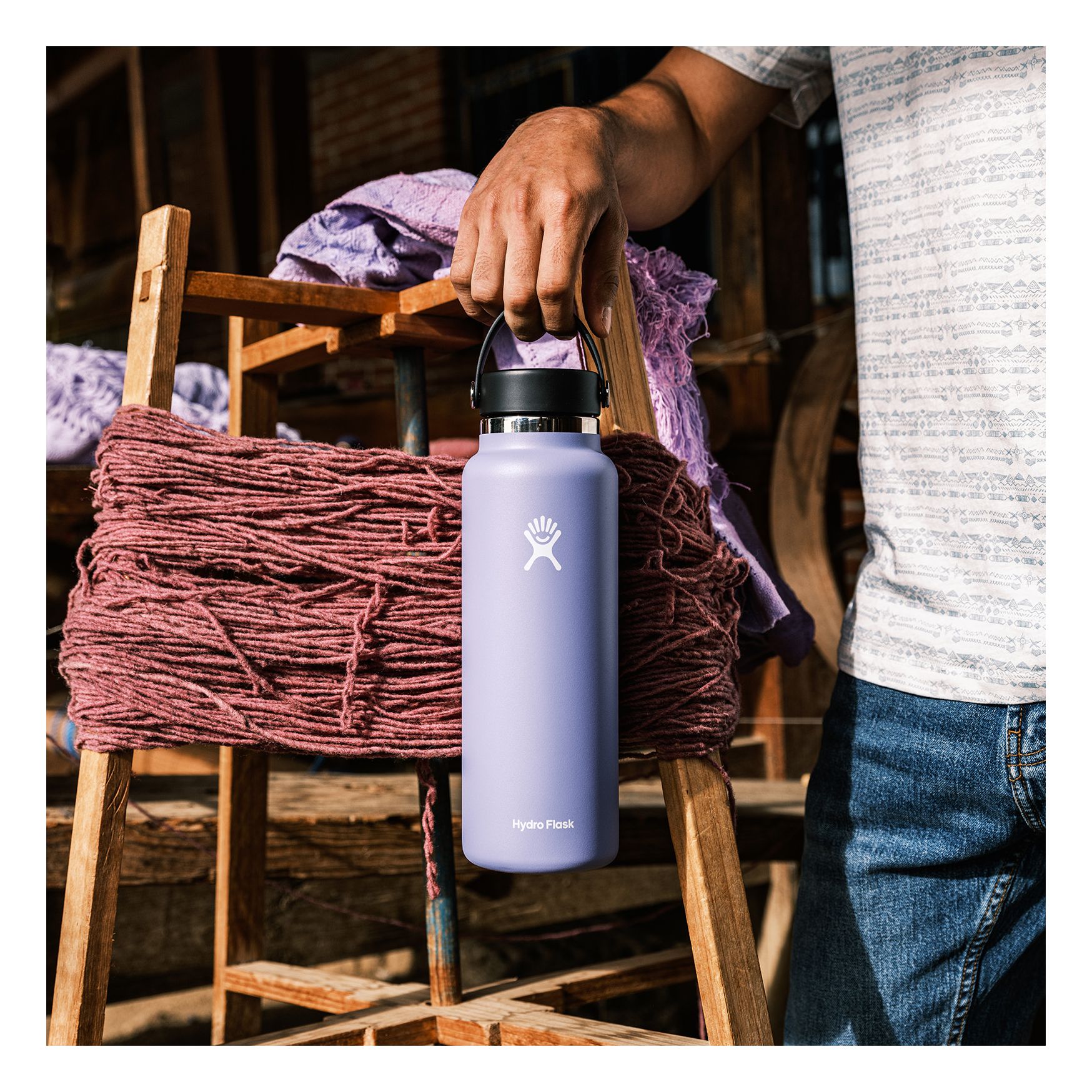 Hand holding a wide-mouth insulated water bottle with flex cap by a wooden ladder with yarn