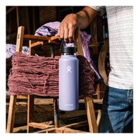 Hand holding a wide-mouth insulated water bottle with flex cap by a wooden ladder with yarn