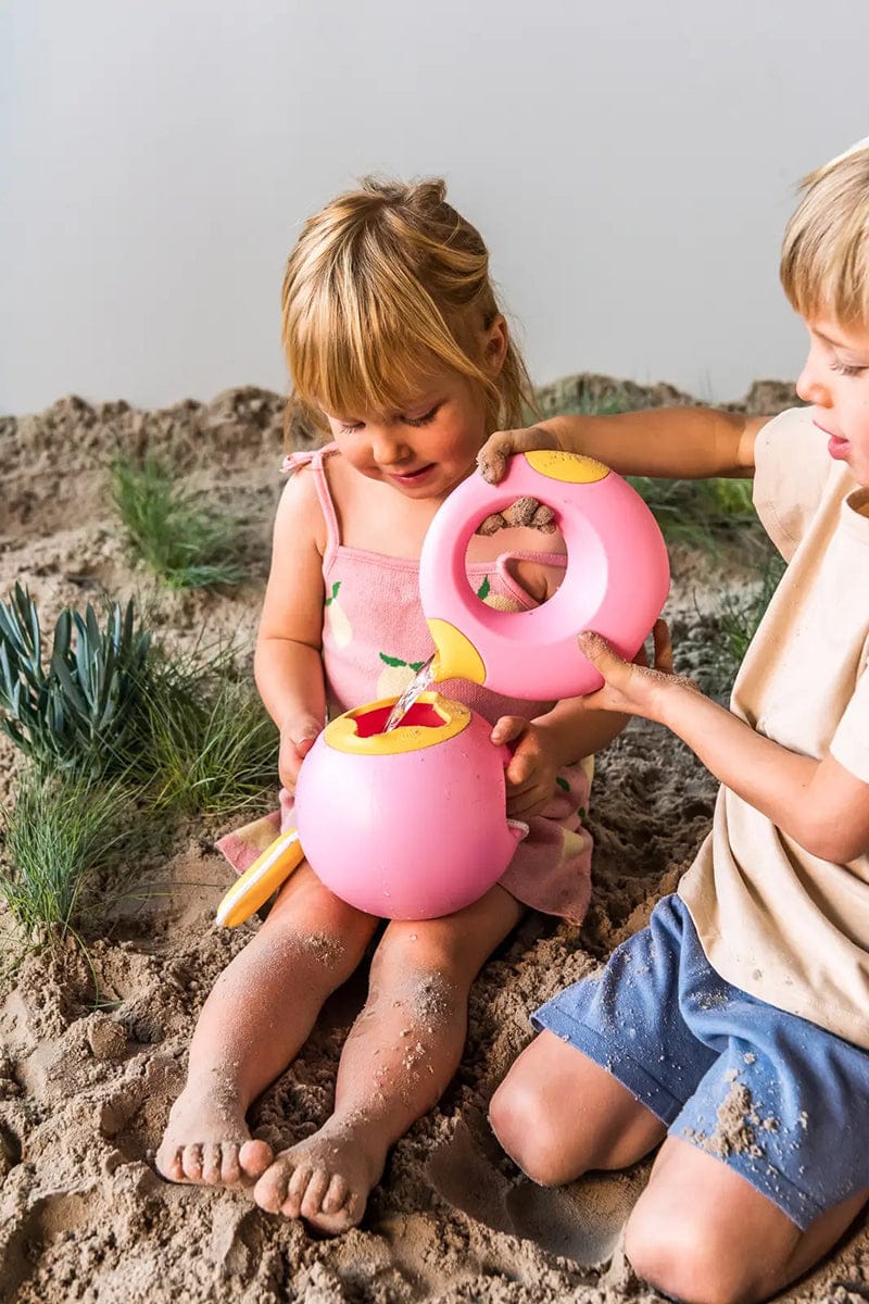 Pink sand and water toy with yellow funnel being used by children on beach