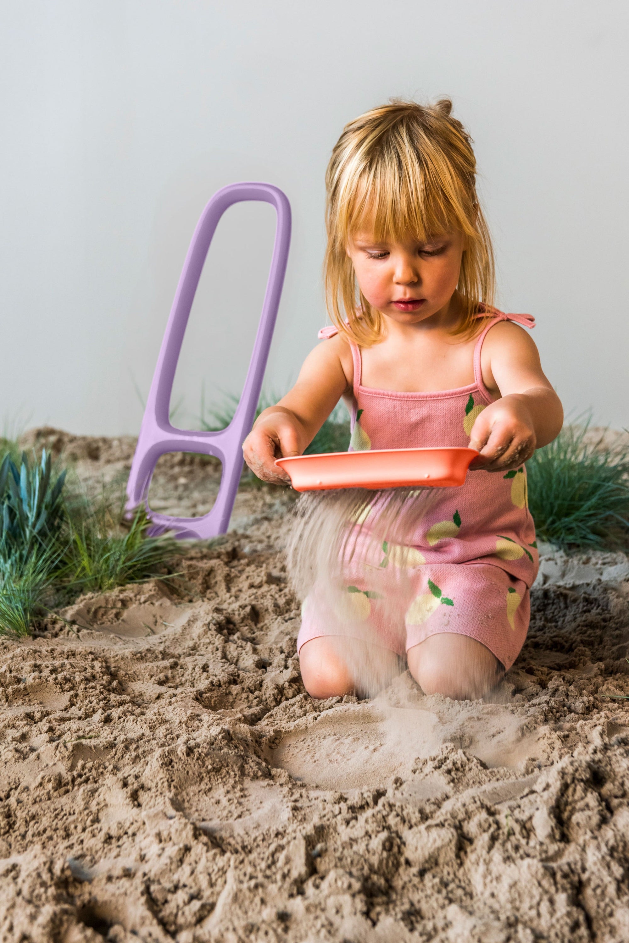 Purple sand sifter toy being used by child in sandbox with sand flowing through