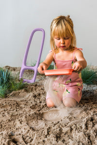 Purple sand sifter toy being used by child in sandbox with sand flowing through