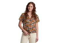 Women's short sleeve button-up top with dark floral print, worn by model with cream pants
