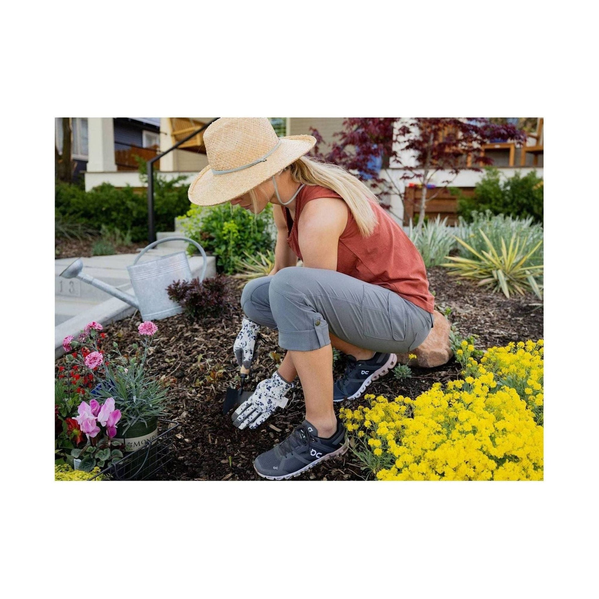 Woman gardening outdoors wearing roll-up capri pants with prosthetic hand, crouched near flowers