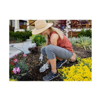Woman gardening outdoors wearing roll-up capri pants with prosthetic hand, crouched near flowers