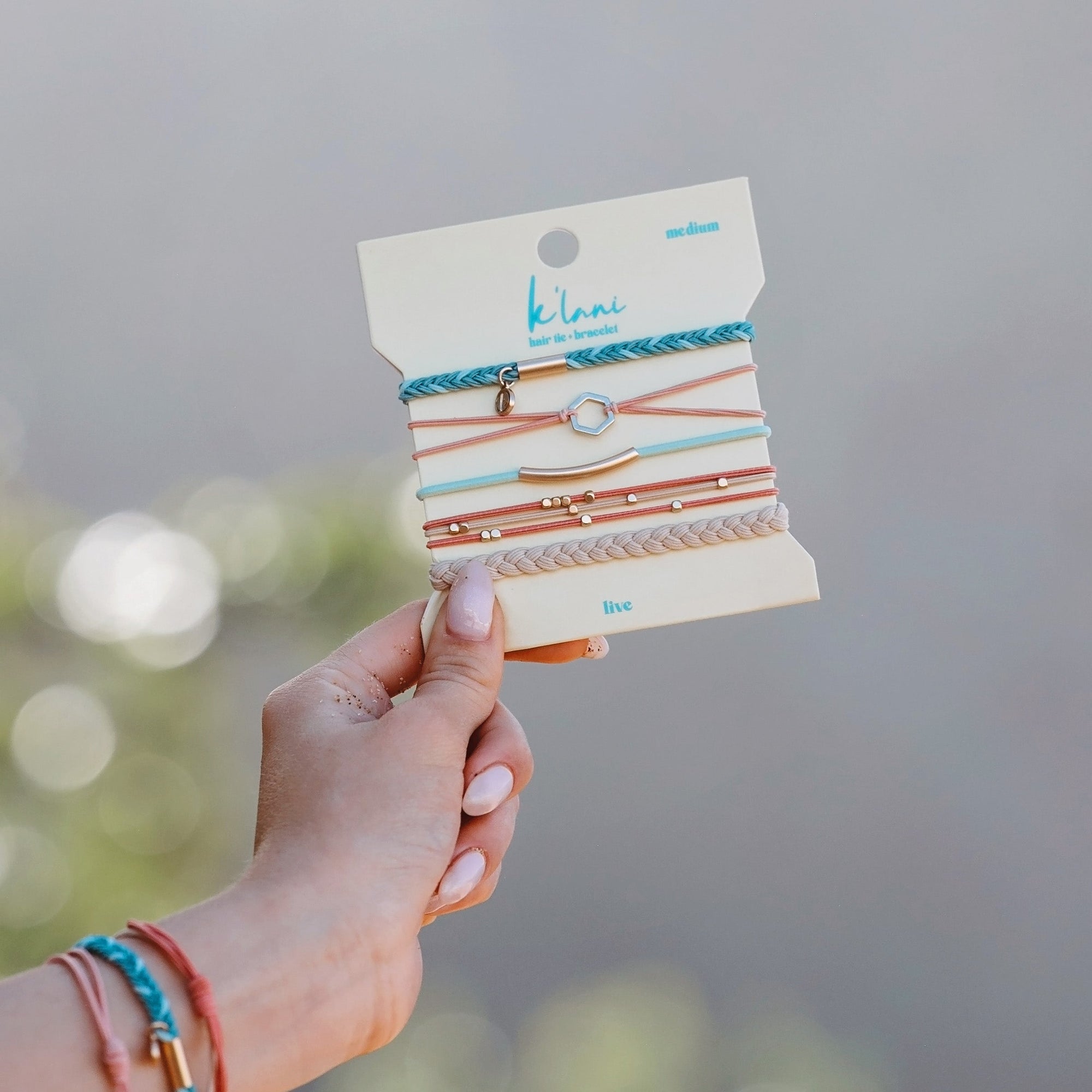 Set of five hair tie bracelets on packaging card, held in hand, featuring braided and cord styles