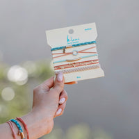 Set of five hair tie bracelets on packaging card, held in hand, featuring braided and cord styles