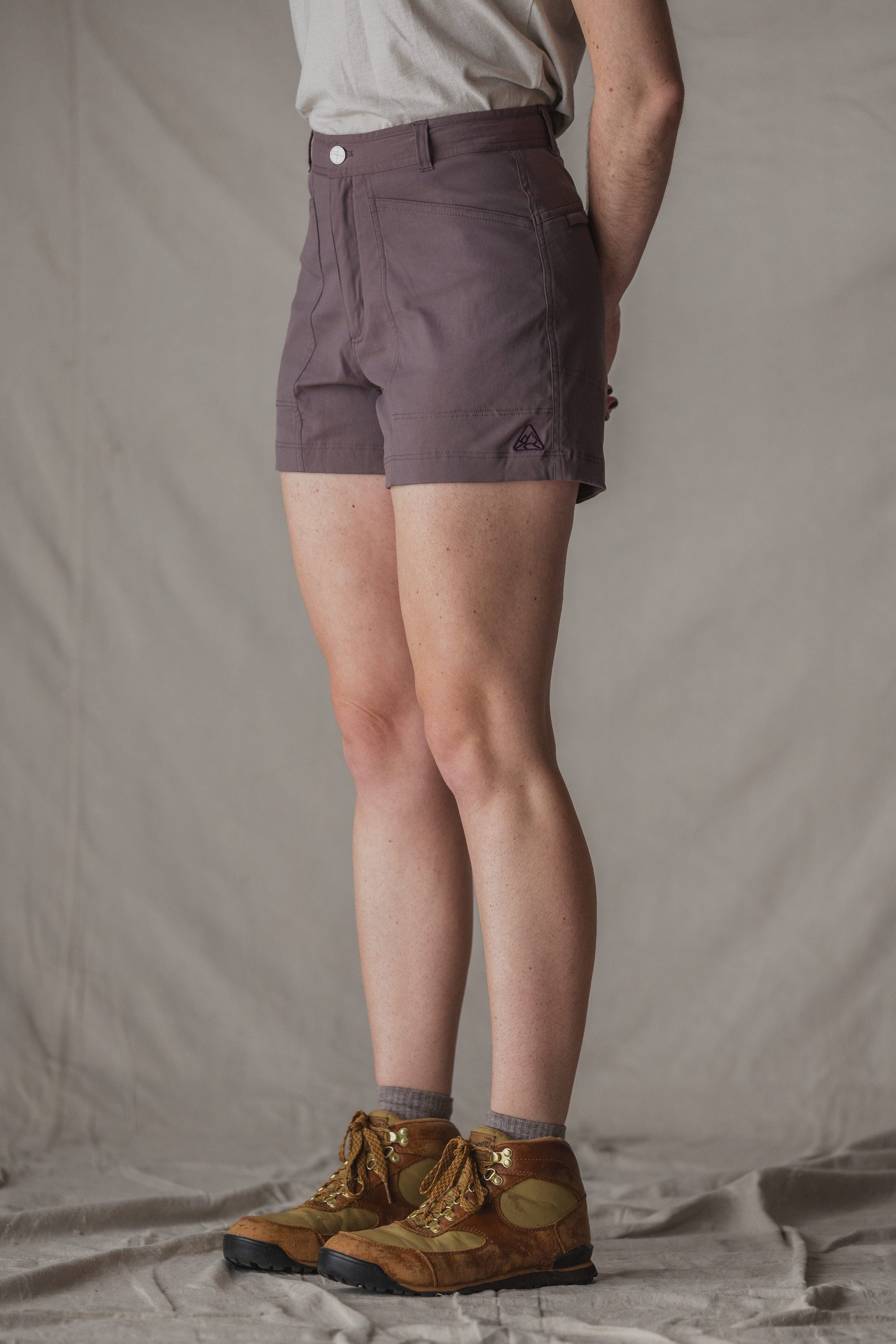 Dark purple trail shorts with button closure and side pockets, worn with hiking boots