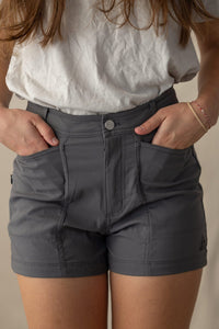 Charcoal gray trail shorts with multiple pockets and button closure, worn by woman