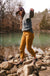 Women's trail pants in warm amber tone, worn on rocky riverbank with sandals, active outdoor setting