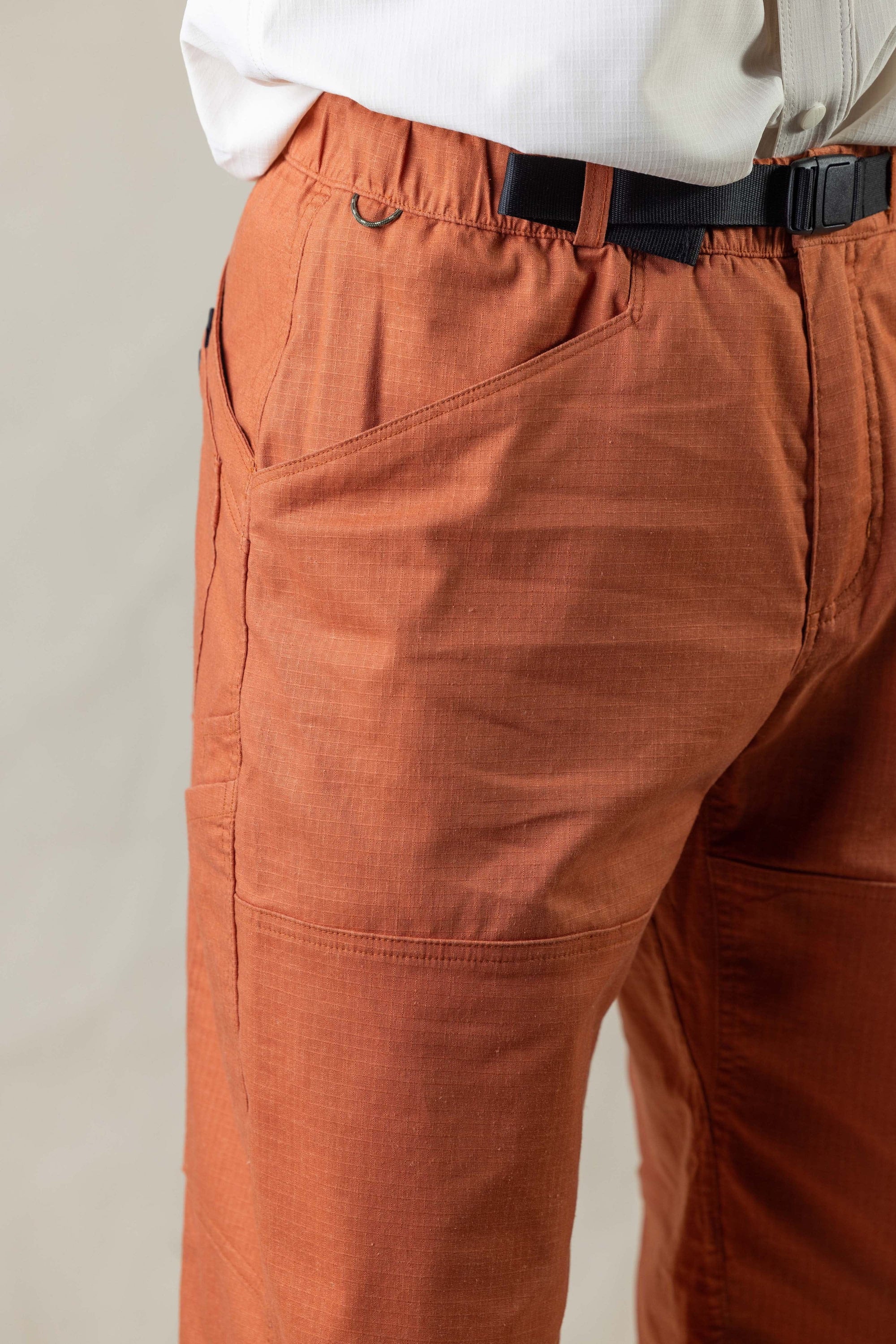 Rust colored outdoor pants with elastic waistband and utility belt, side angle view