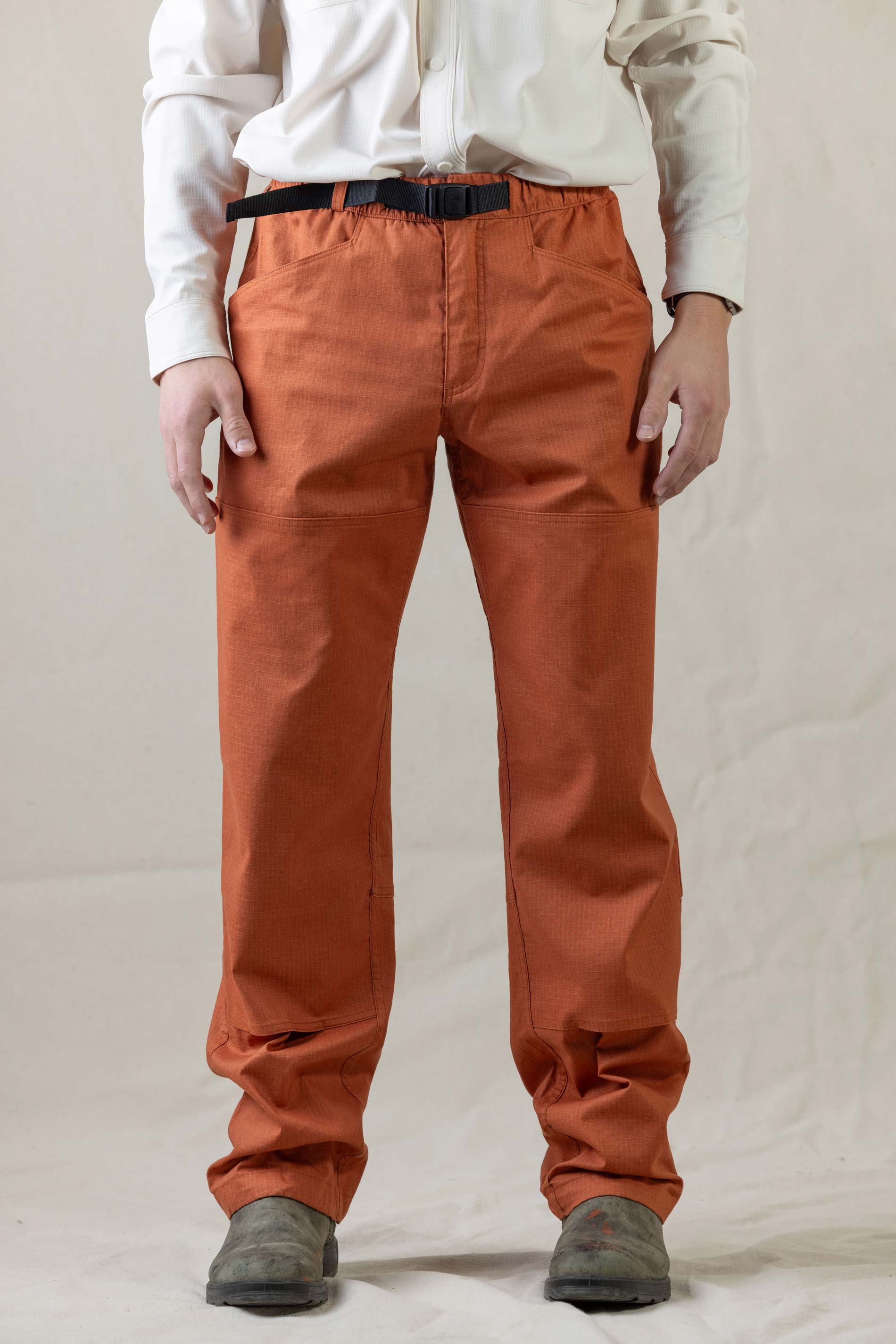 Rust colored outdoor pants with black belt and reinforced knee panels, front view