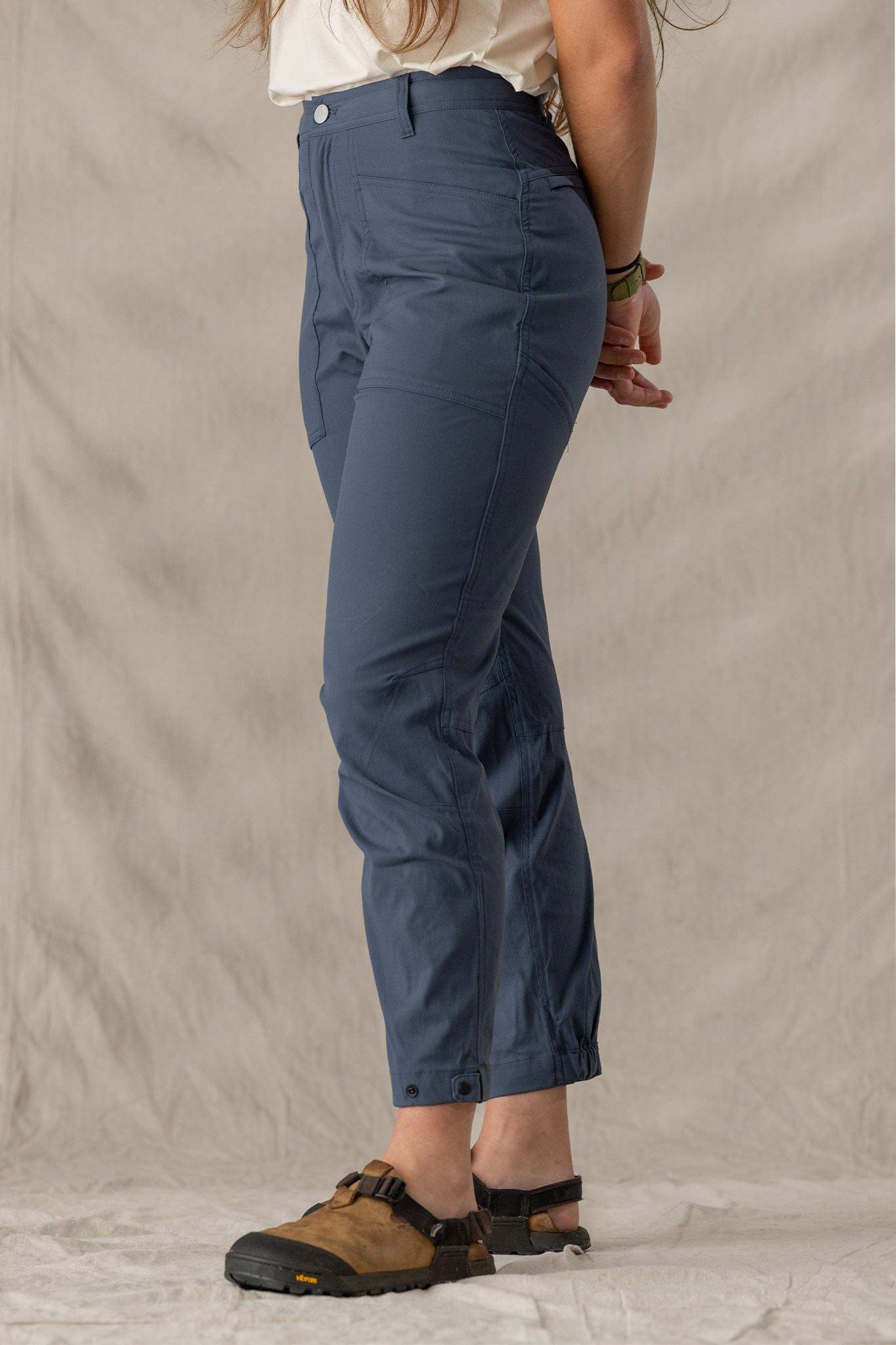 Women's cropped trail pants in dark blue-gray, side view, with snap hem detail and sandals