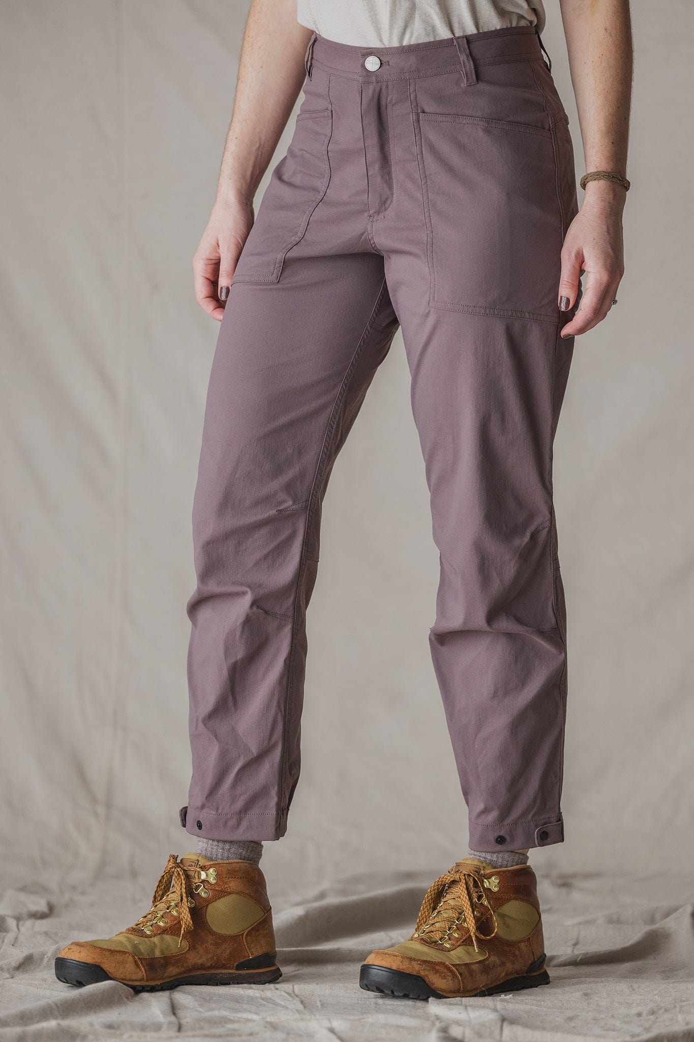 Women's trail pants in dusty mauve with front pockets and snap cuffs, paired with hiking boots