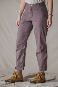 Women's trail pants in dusty mauve with front pockets and snap cuffs, paired with hiking boots