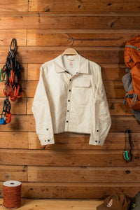 Off-white button-front jacket with chest pocket and snap closures, hung on wooden wall