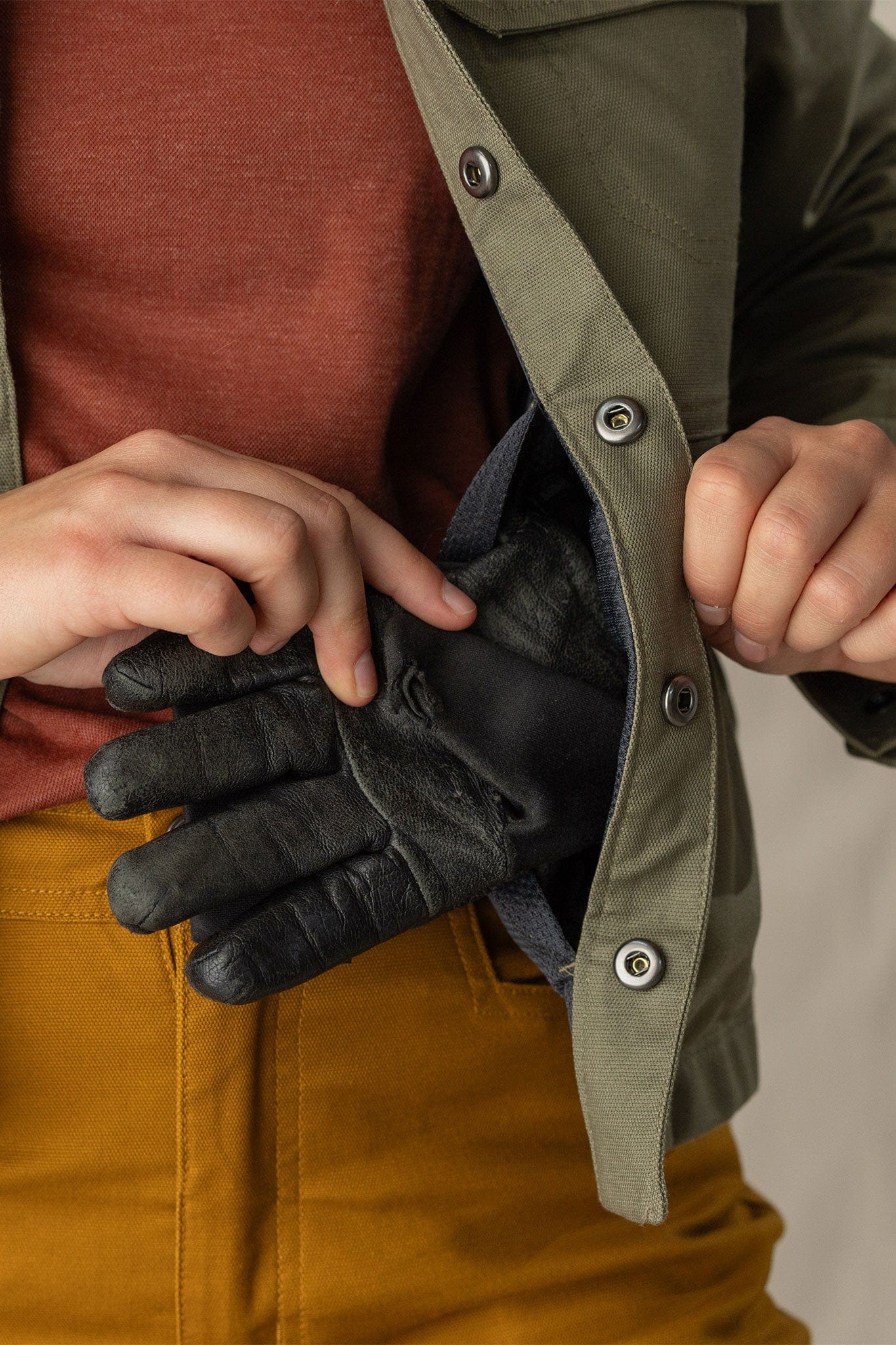 Close-up detail of olive jacket interior pocket holding black leather gloves, snap button placket visible