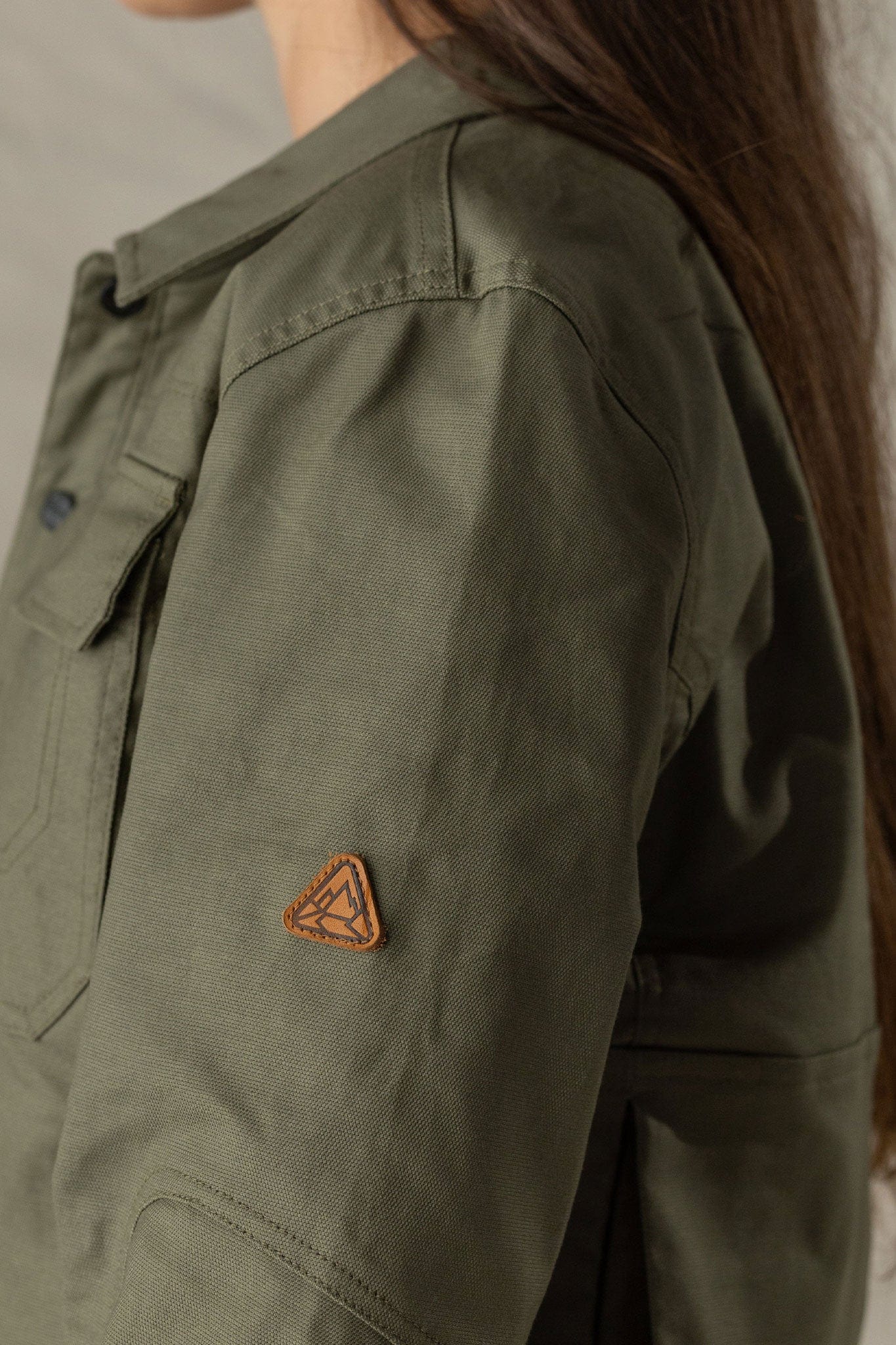 Close-up detail of olive green women's jacket sleeve with leather triangle brand patch