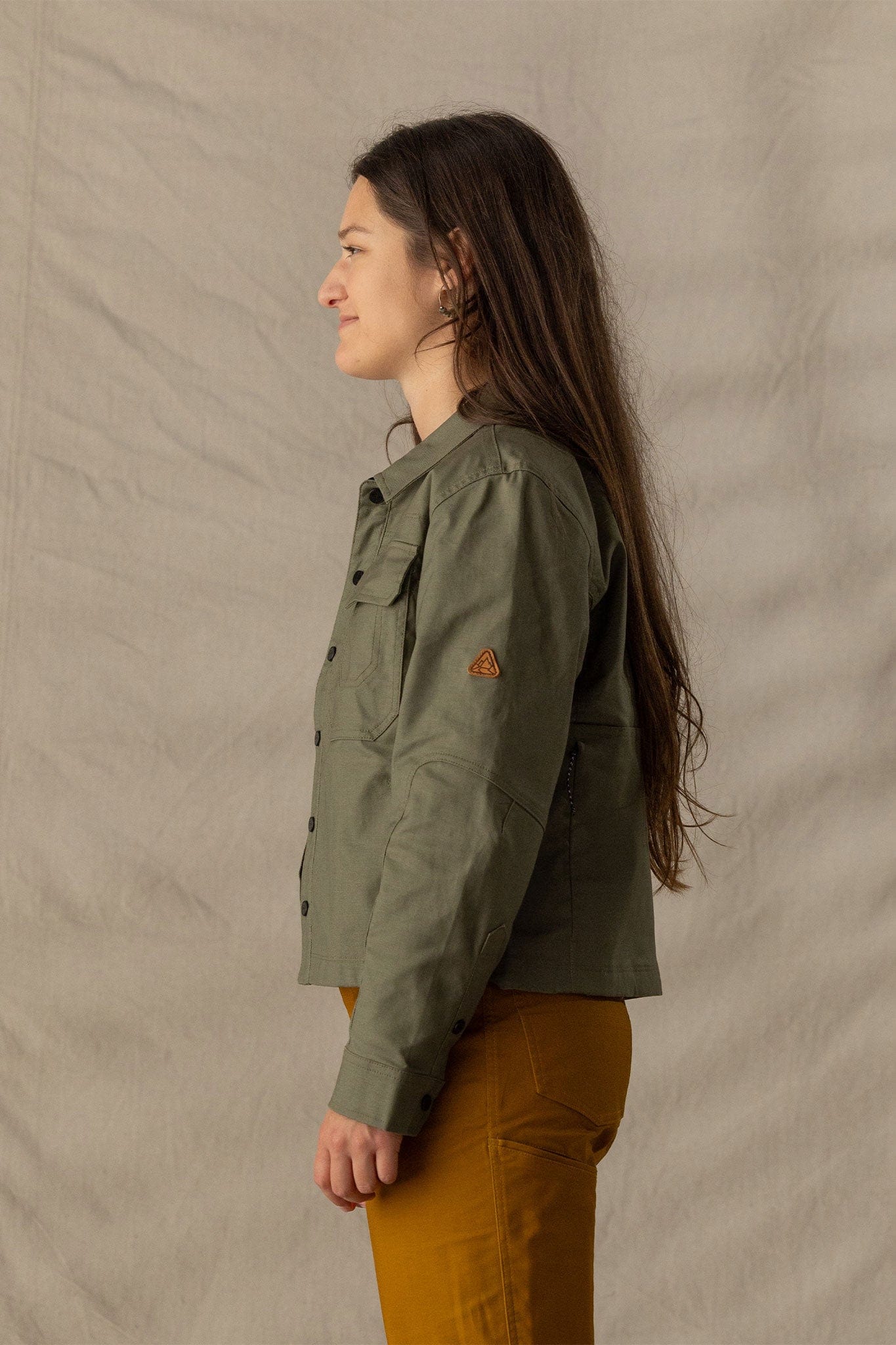 Women's military-style olive jacket with chest pockets and snap buttons, side view on model