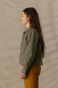 Women's military-style olive jacket with chest pockets and snap buttons, side view on model