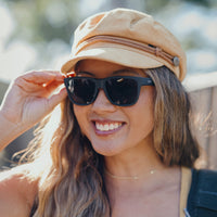 Woman wearing black sunglasses and beige cap, smiling outdoors in bright sunlight