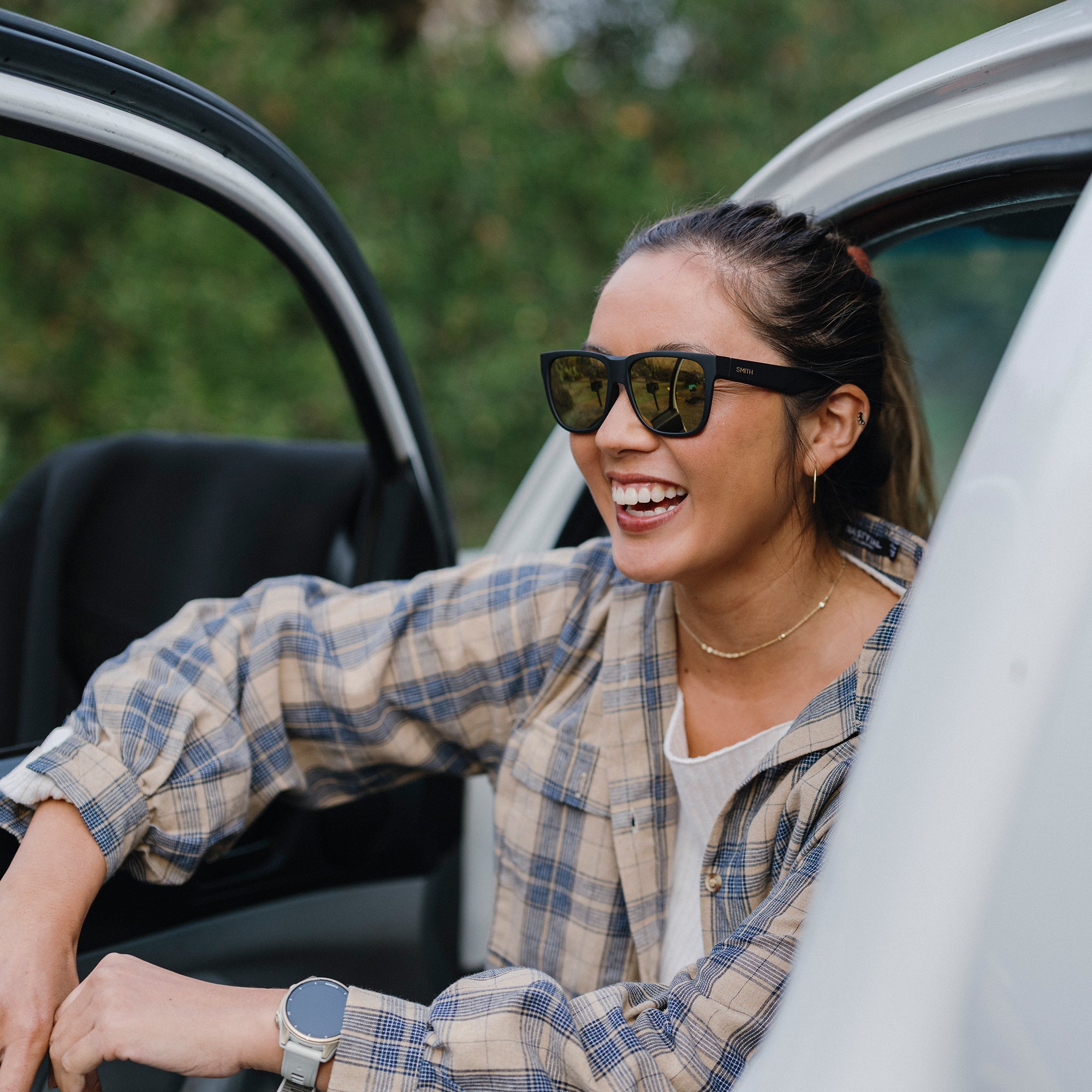 Woman wearing black sunglasses with mirrored lenses leaning out of white car door