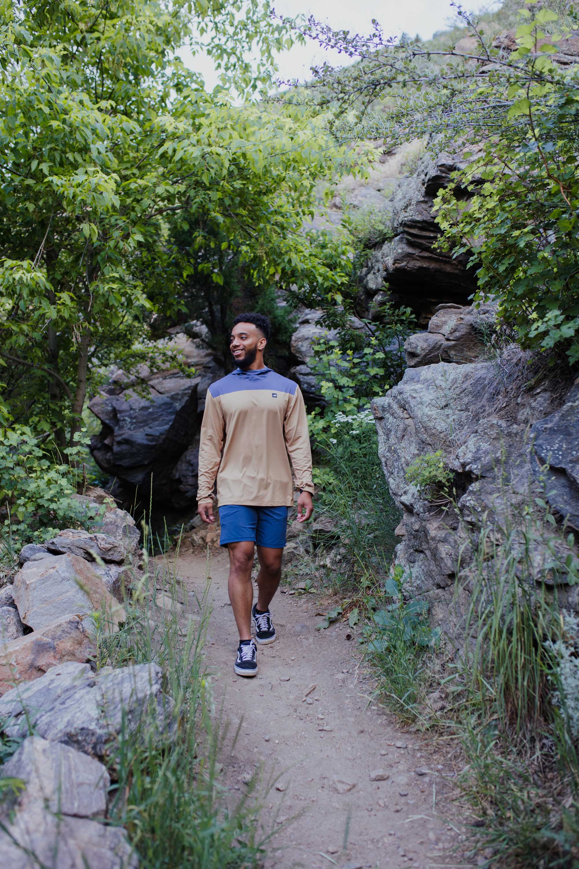 Man wearing brown and blue color block long sleeve hoodie while hiking on rocky trail