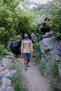 Man wearing brown and blue color block long sleeve hoodie while hiking on rocky trail