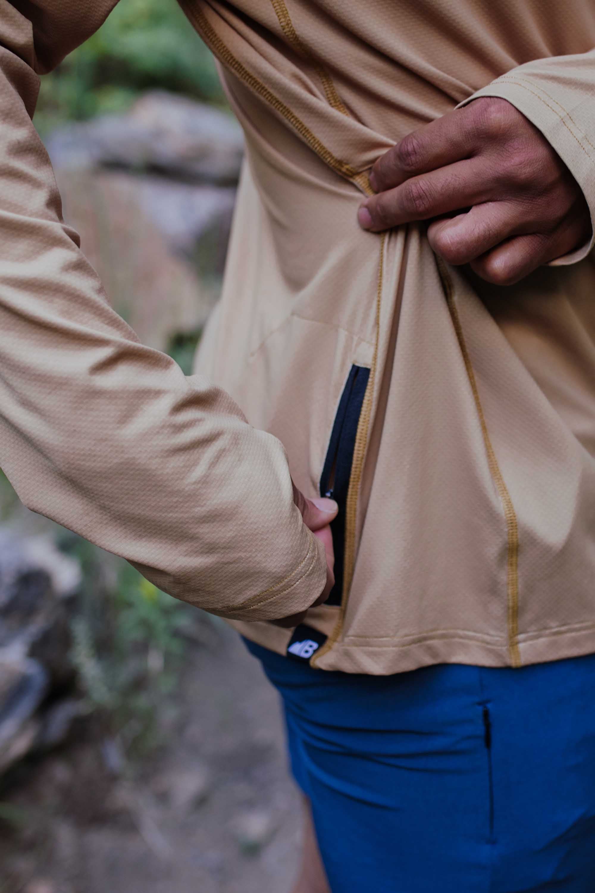 Man wearing brown zip-up hoodie with blue pants, showing interior pocket detail
