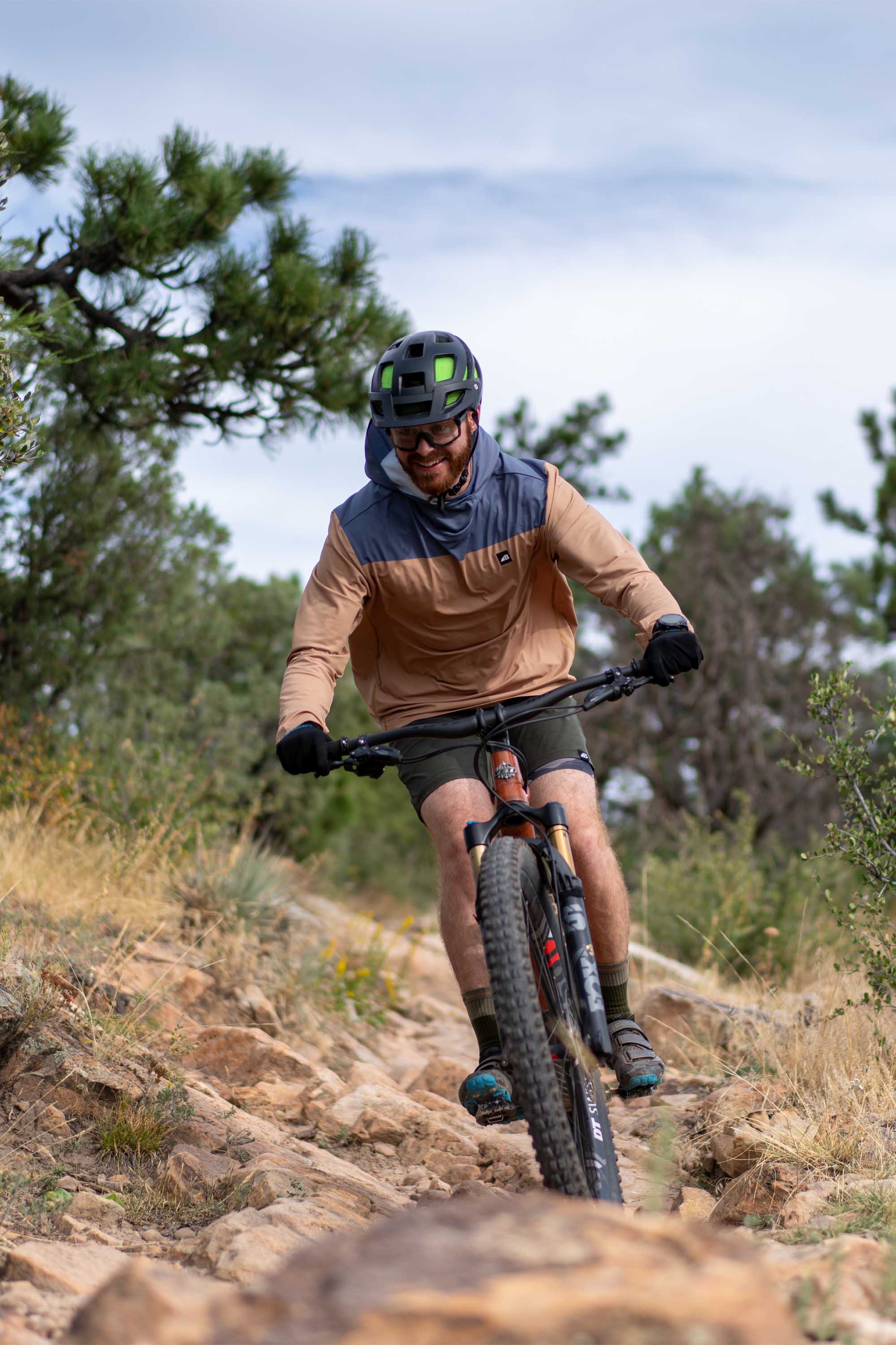 Man wearing brown and blue color-blocked hoodie while mountain biking on rocky terrain