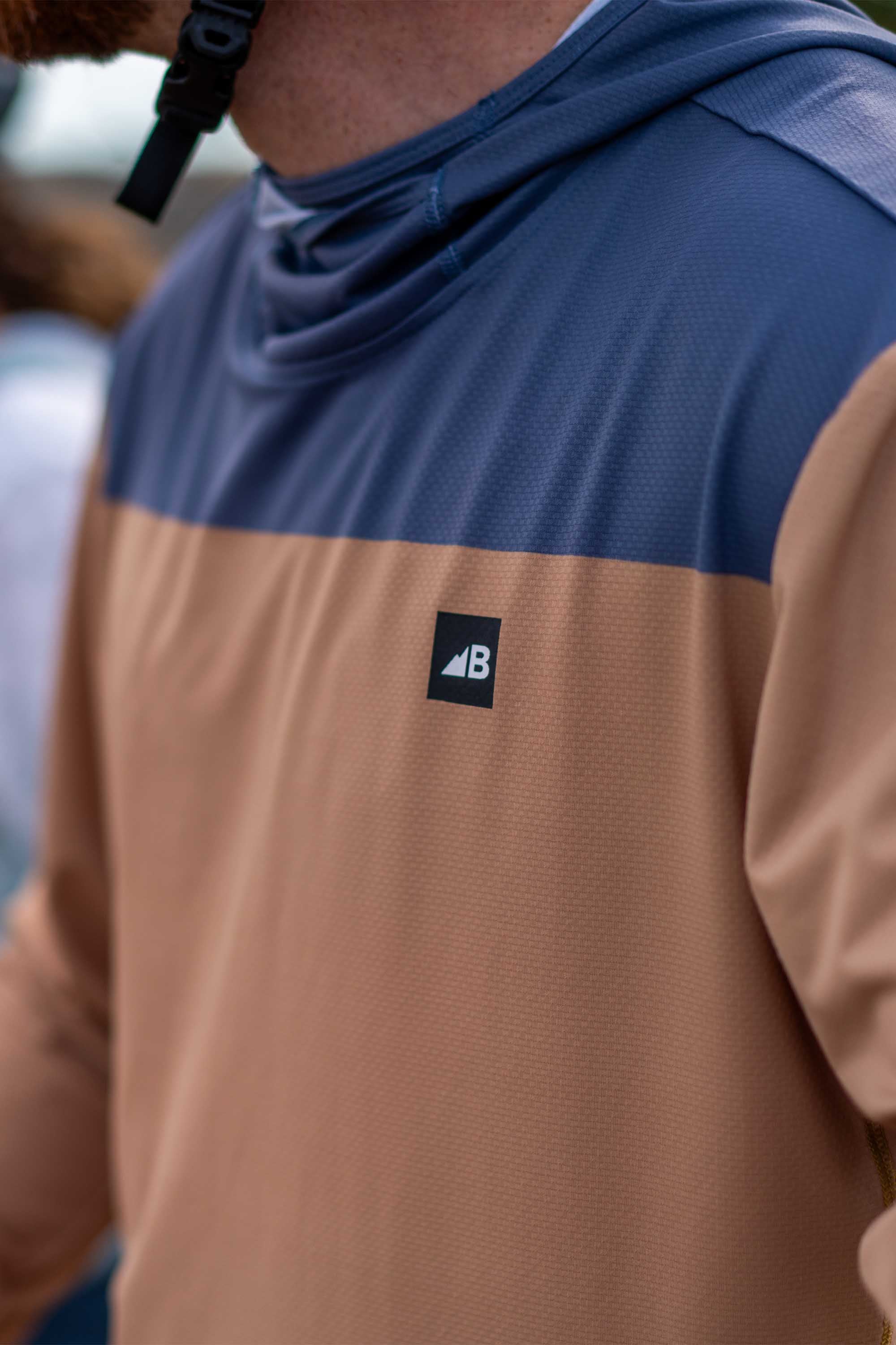 Color-blocked hooded sun shirt with navy blue top panel and brown bottom panel, worn outdoors