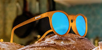 Orange-framed sunglasses with blue mirrored lenses resting on textured brown surface