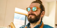 Orange-framed sunglasses with mirrored lenses worn by bearded man in lifestyle setting