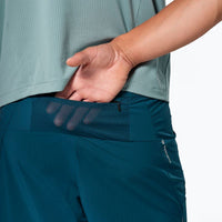 Teal athletic shorts with mesh back pocket detail, worn by person from waist down