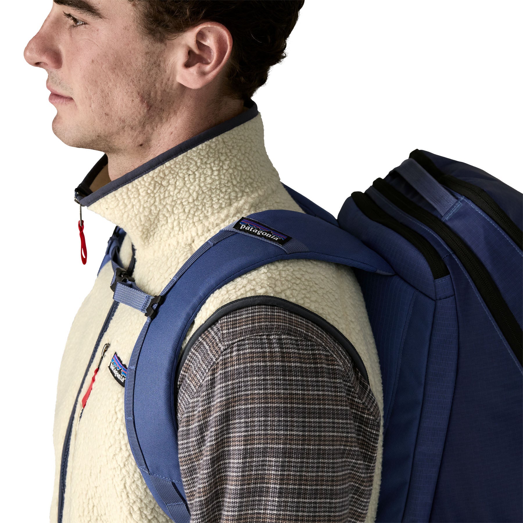 Men's sherpa fleece vest in cream, worn over plaid shirt with navy backpack, side view
