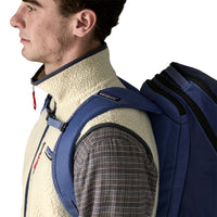 Men's sherpa fleece vest in cream, worn over plaid shirt with navy backpack, side view