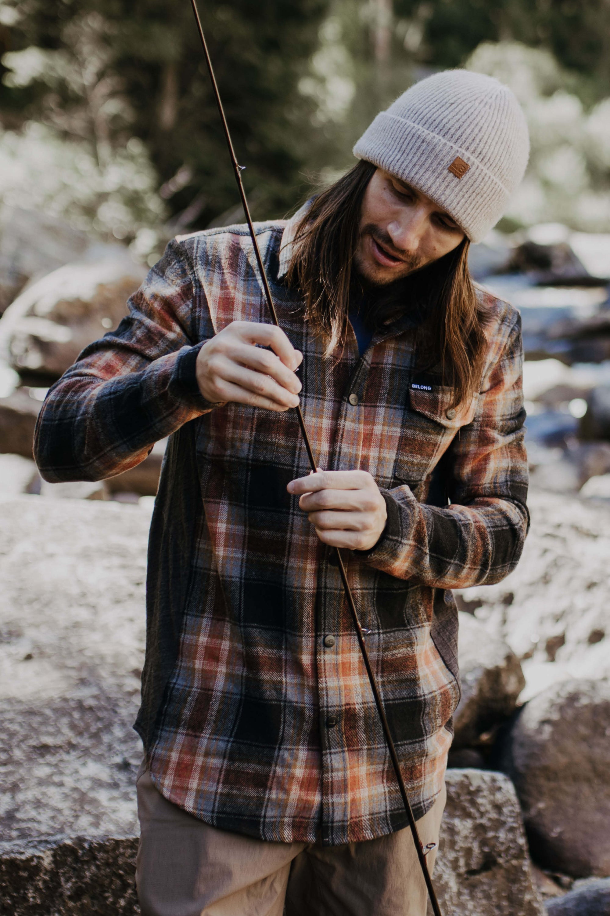 Man wearing a light beige ribbed knit beanie while preparing a fishing rod outdoors