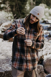 Man wearing a light beige ribbed knit beanie while preparing a fishing rod outdoors