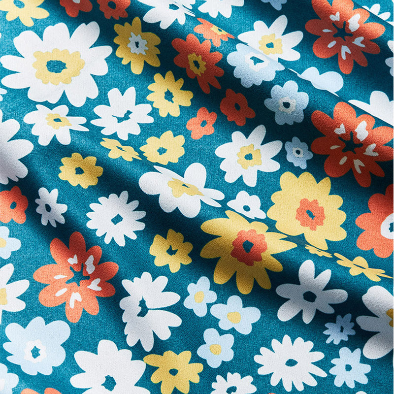 Folded fabric towel with teal background and colorful daisy flower pattern, close-up detail view