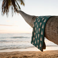 Patterned beach towel draped over palm tree trunk with ocean and sunset in background
