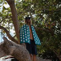 Teal patterned towel worn as cape by person standing on tree branch outdoors